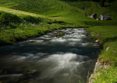 Foto: Langzeitaufnahme eines Flusses, eingebetet in grüne Wiesen