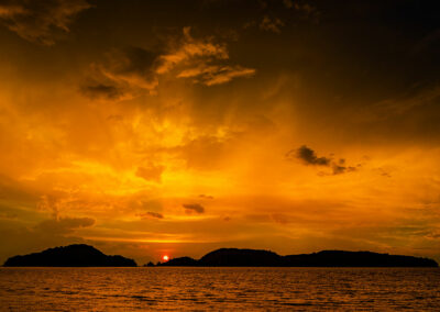 Foto: hinter einer Insel untergehende Sonne lässt Himmer und Wasser goldig leuchten